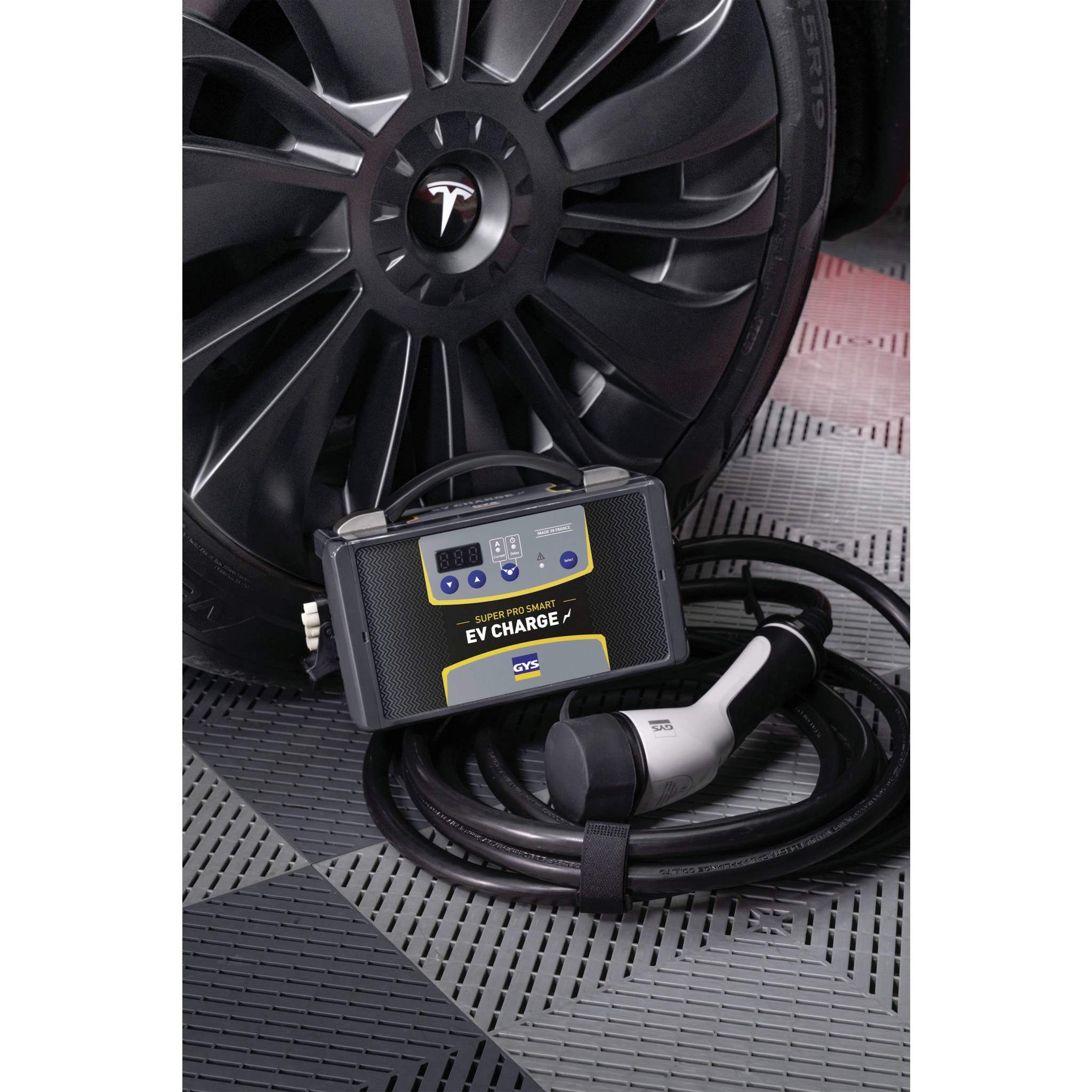 An electric vehicle charging cable lies on the ground next to a car with a large wheel visible. A display shows 'EV Charge'.