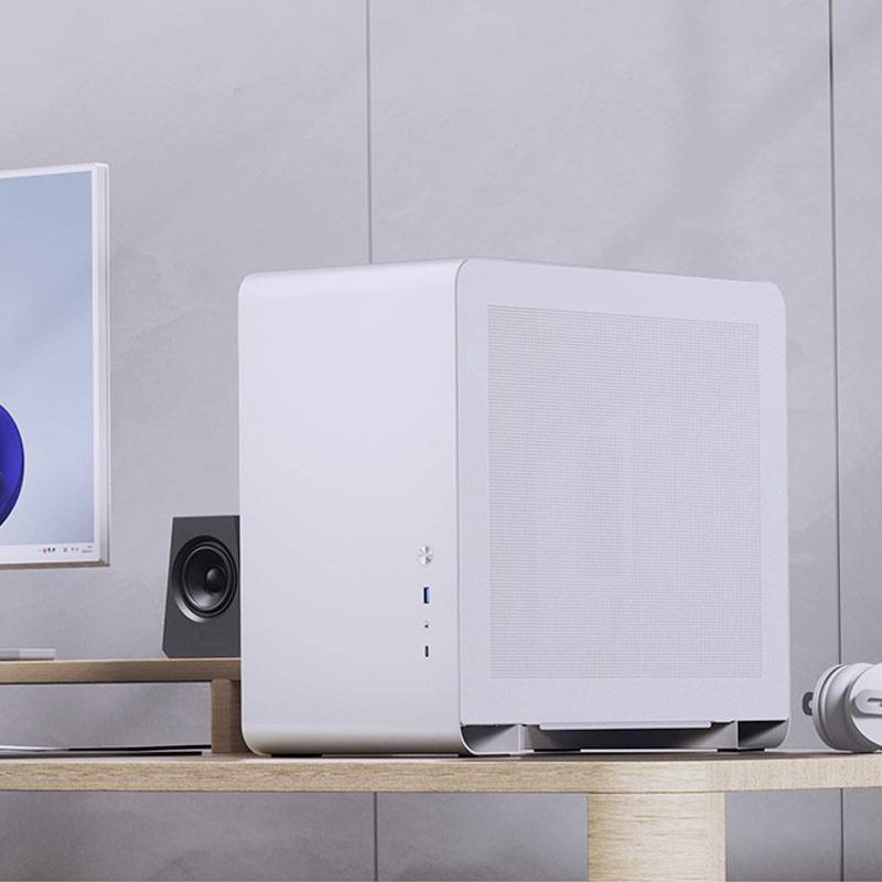 A minimalist computer on a wooden table, beside a screen and speakers, points to a modern work environment.