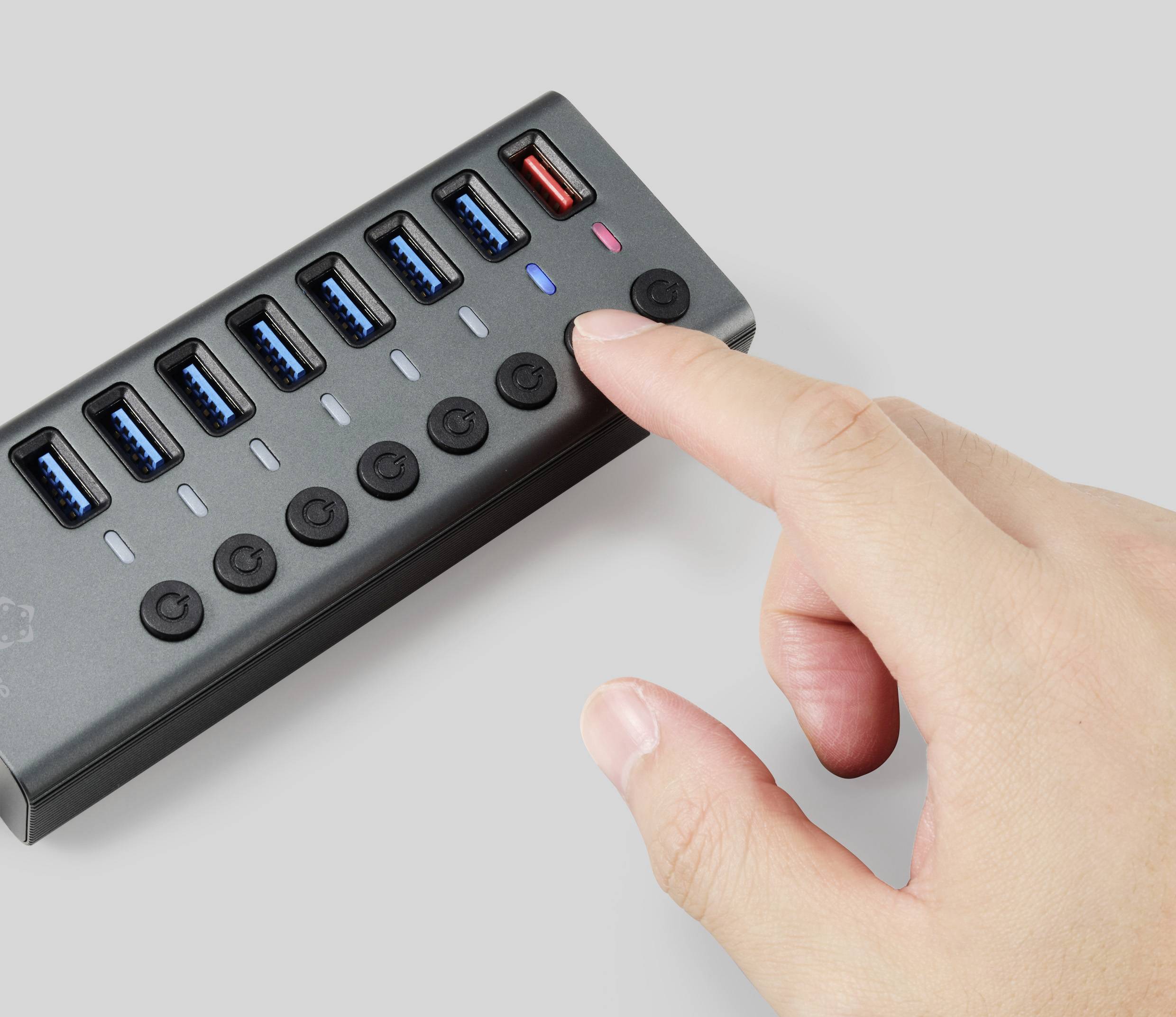 A hand is pointing at a USB hub with multiple ports and power buttons. A red USB port stands out from the others.