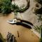 A pair of secateurs lies on a table, surrounded by pine branches and raffia, suggesting creative crafting or floristry.