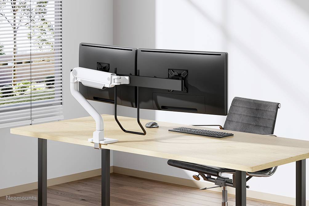 Two large monitors mounted on a dual-arm mount, positioned on a modern desk with a keyboard and ergonomic chair in the office.