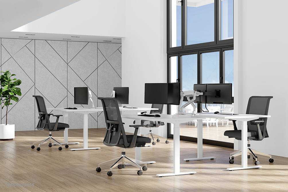 A modern, light-filled office with four desks and computers. Large windows allow plenty of natural daylight to enter.