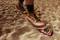 A large boot treads on a red toy car in the sand, partially crushed beneath the shoe.