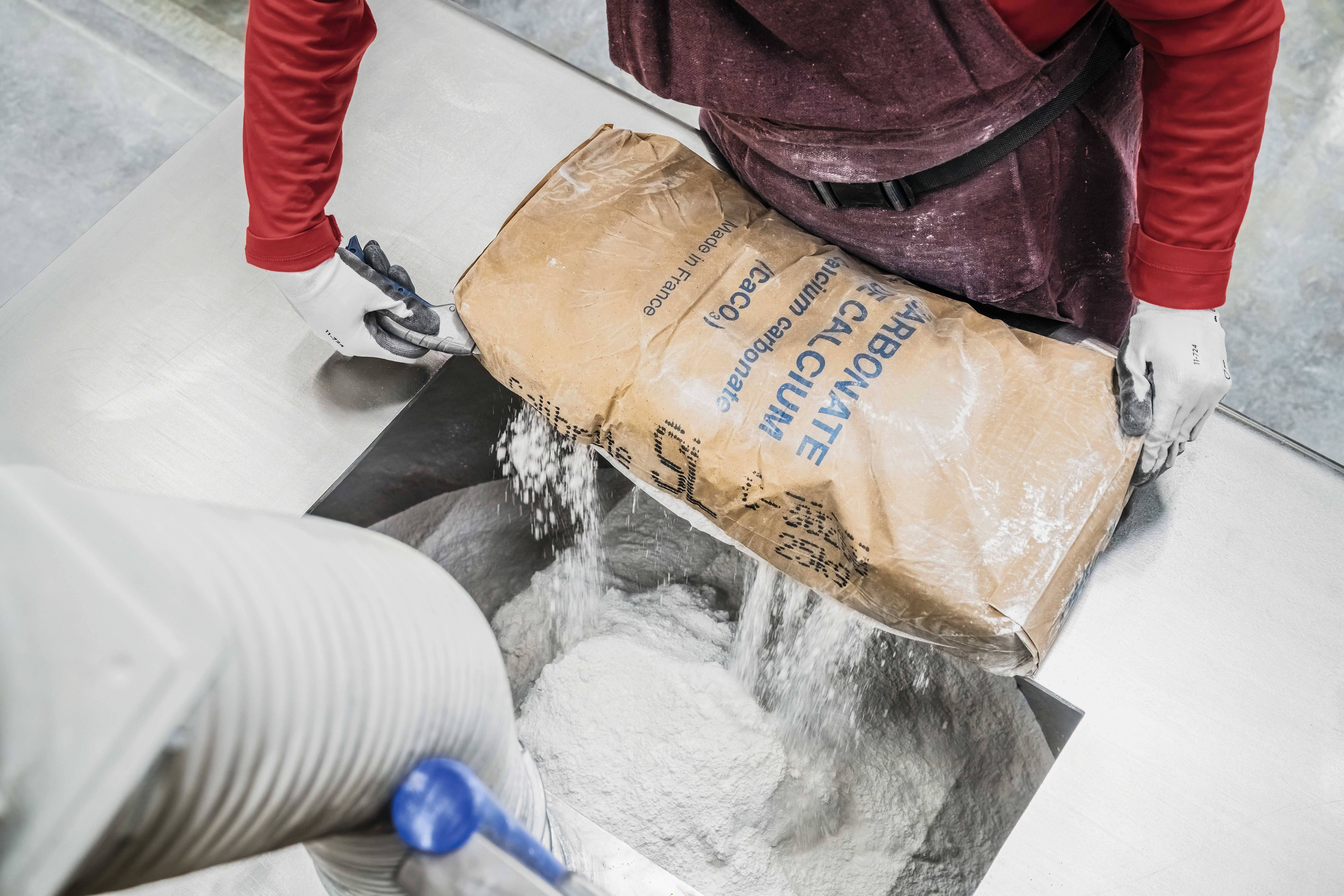A person is pouring a white powder bag into a machine.