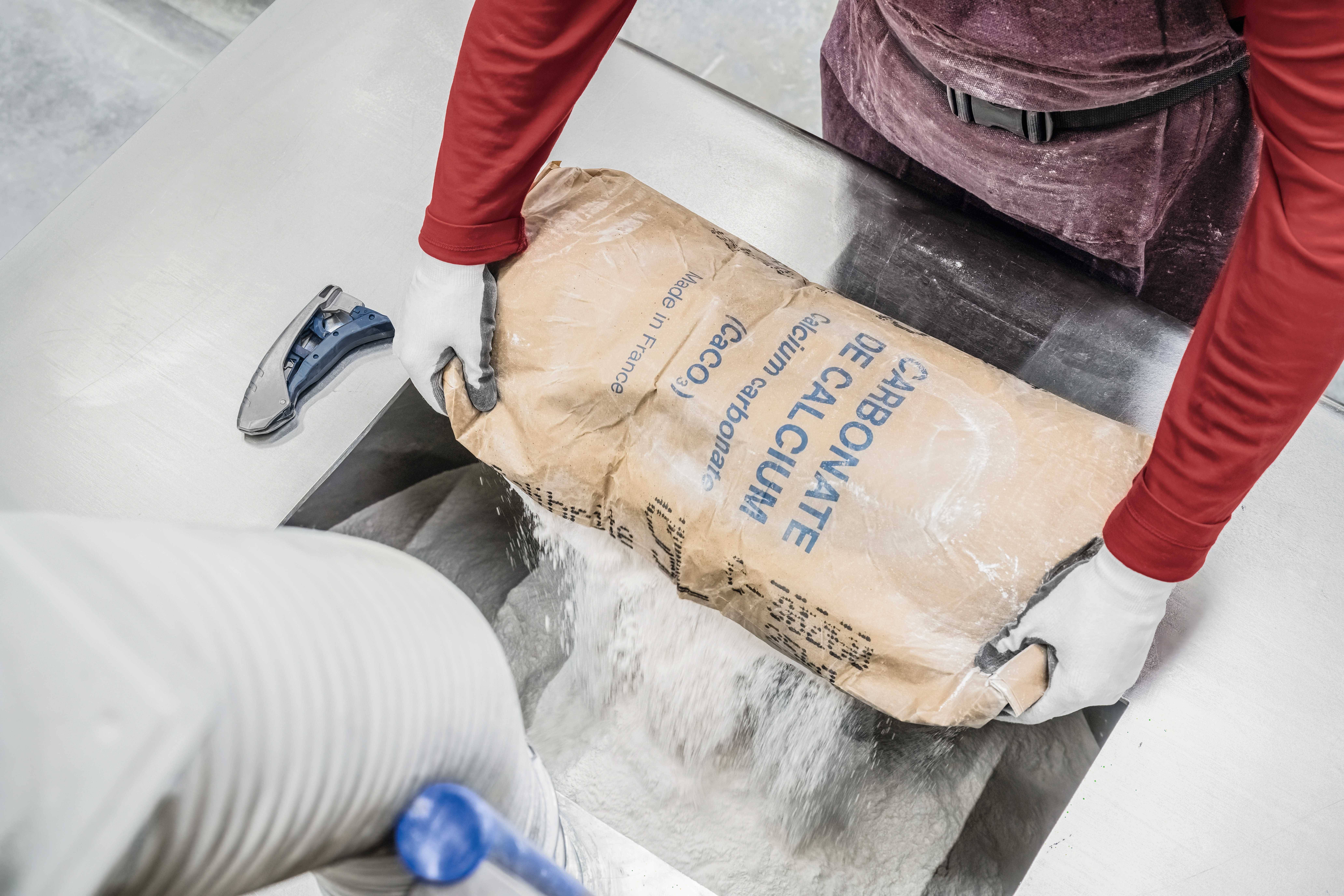 'Worker pours calcium powder from a sack into a machine.'