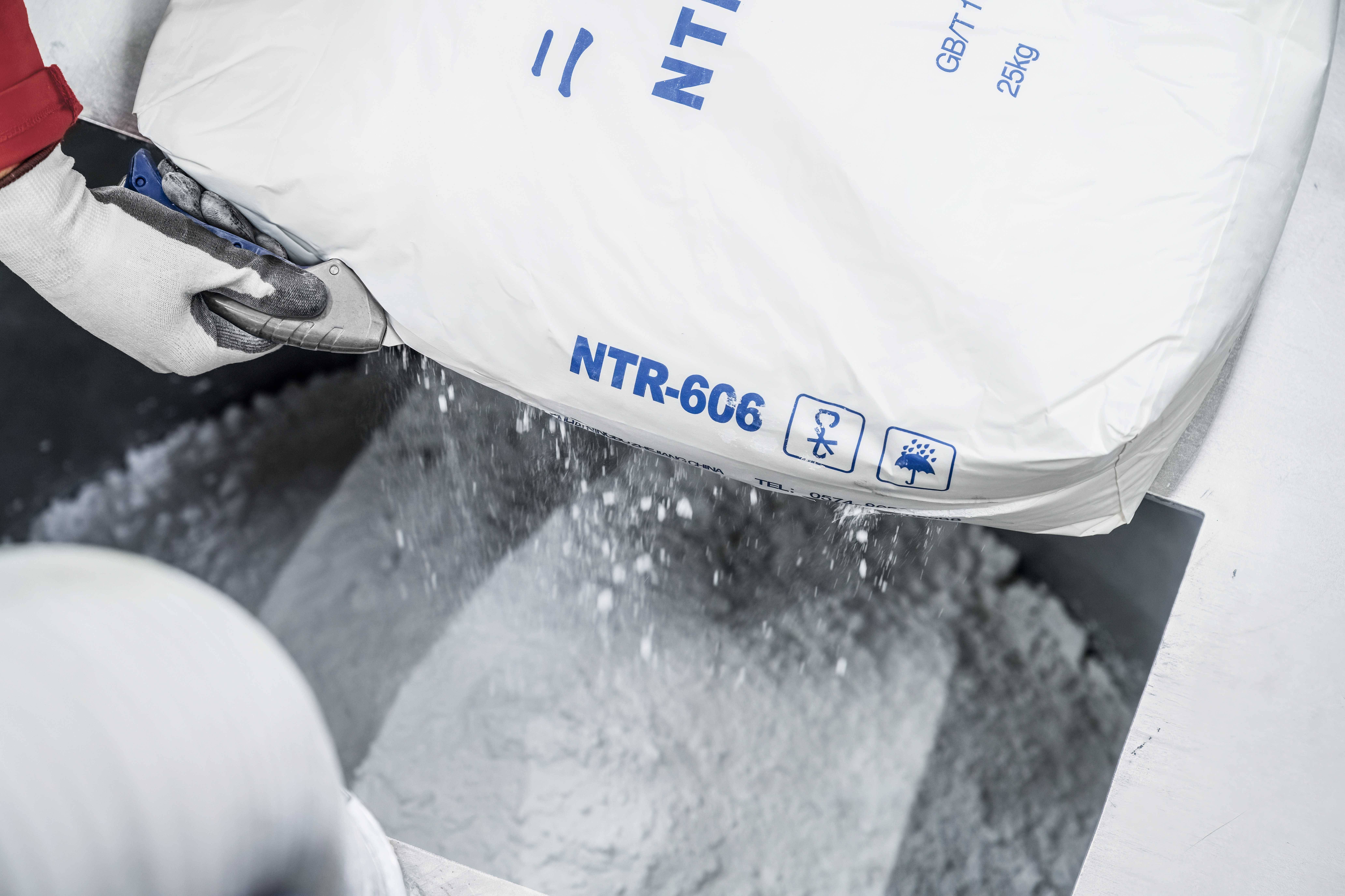 'A person is pouring white powder contents from a sack labelled "NTR-666" into a metal funnel.'