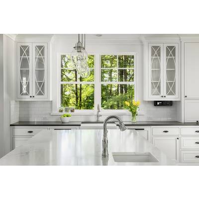 Bright, modern kitchen with white cabinets, marble island and large window offering a view of green trees. Yellow tulips on the worktop.