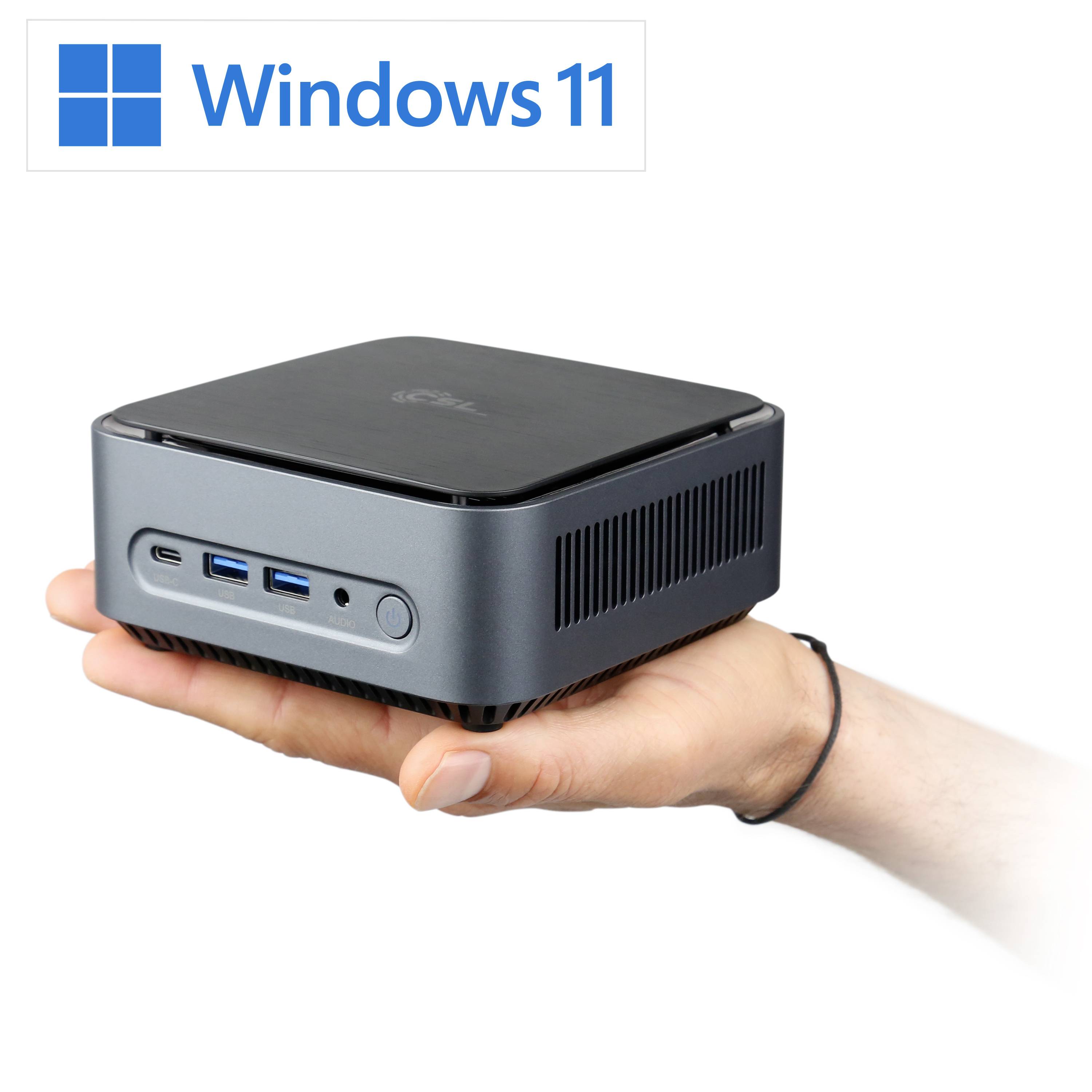 A hand is holding a compact mini PC with multiple USB ports. The Windows 11 logo is displayed on top.