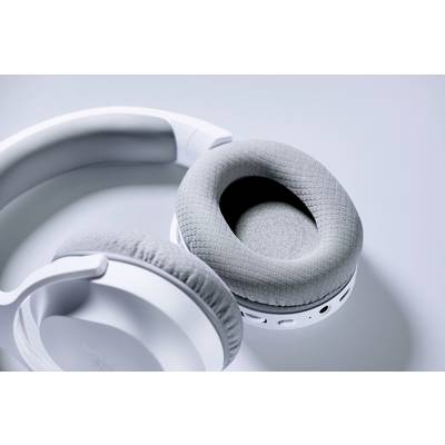White, wireless headphones are lying on a grey surface. They are closed and visible on the left side.