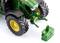 A green tractor with large tyres stands on a white background. A green counterweight lies in front of the vehicle.