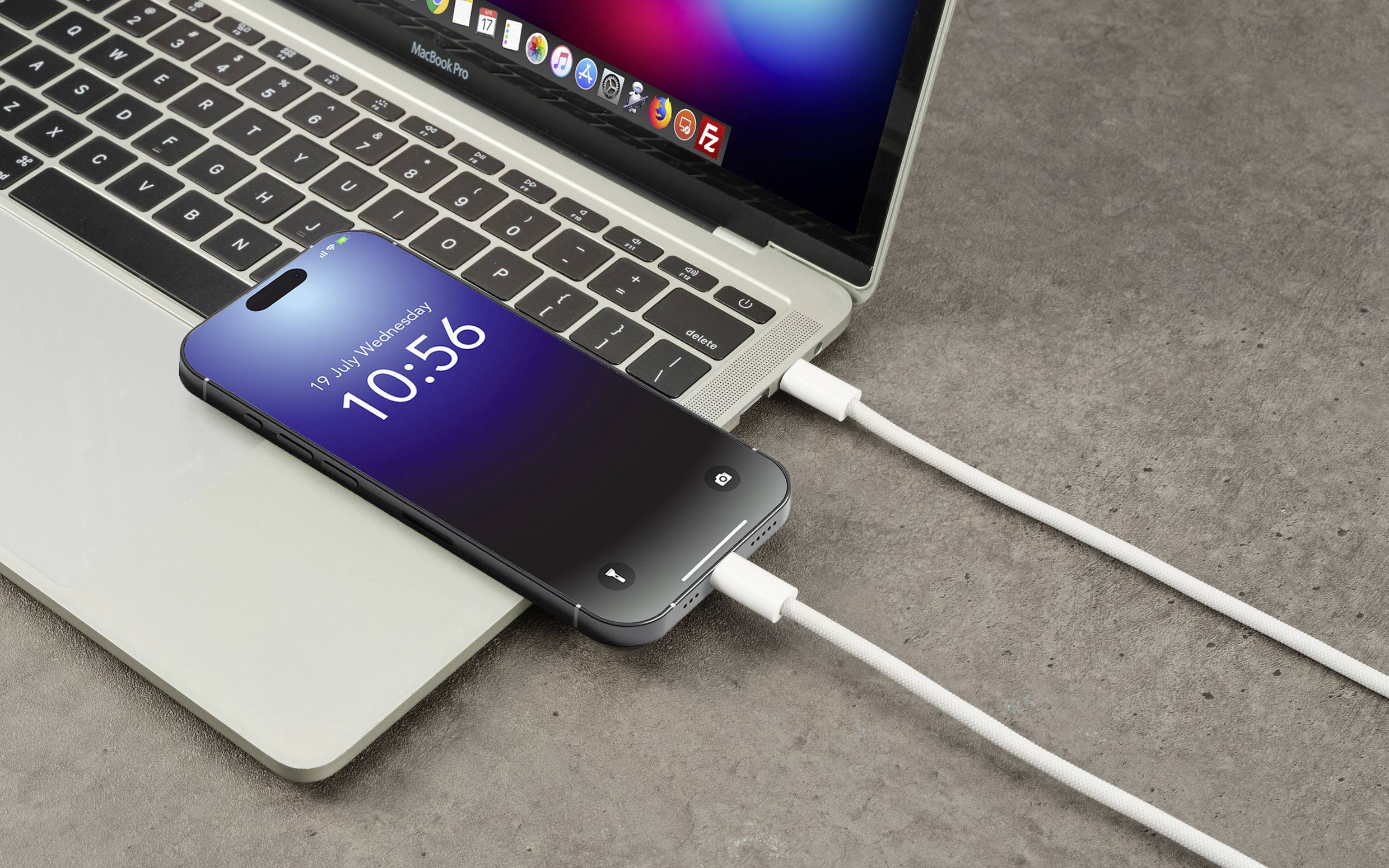 A smartphone is lying on a laptop and being charged via cable. Both devices are switched on. Time on the smartphone display: 10:56.
