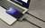 A smartphone is connected to a laptop via a black cable. The phone screen displays the time '10:56'.