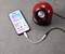 A smartphone is playing a song and is connected via a cable to a red, spherical speaker.