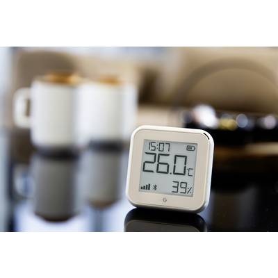 Digital thermo-hygrometer displays 26.0°C and 39% humidity, with blurred cups in the background.