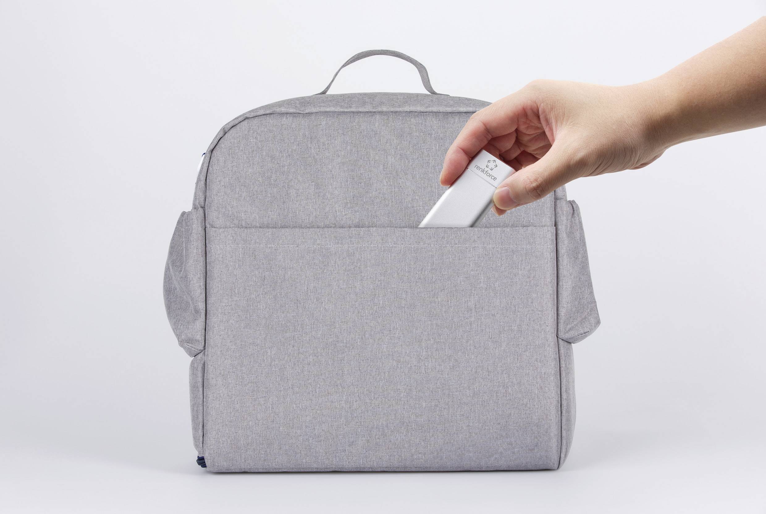 A hand places a USB stick into the front pocket of a grey rucksack.