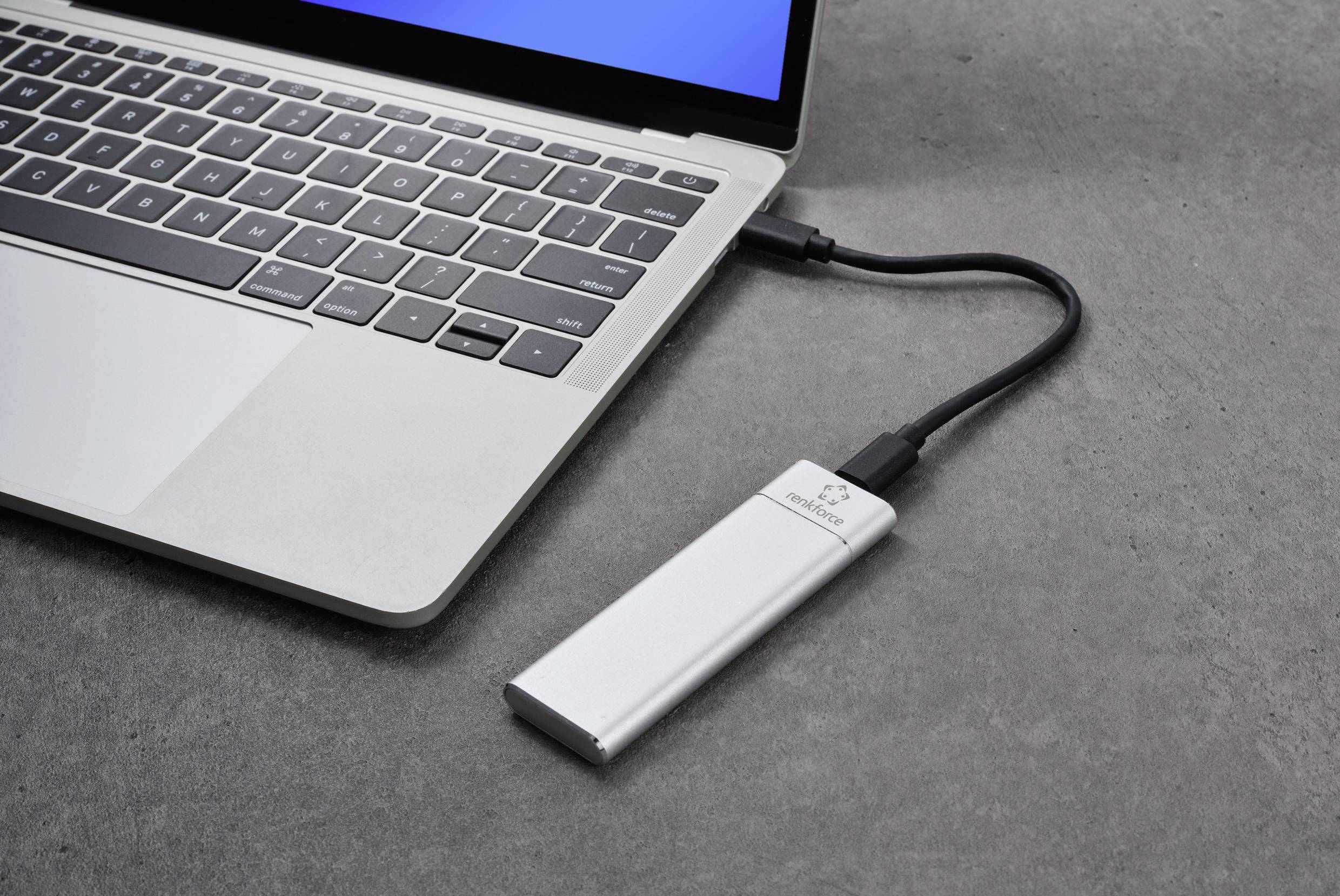 An external storage device is connected to a laptop via a cable. The laptop screen shows the beginning of a blue user interface.