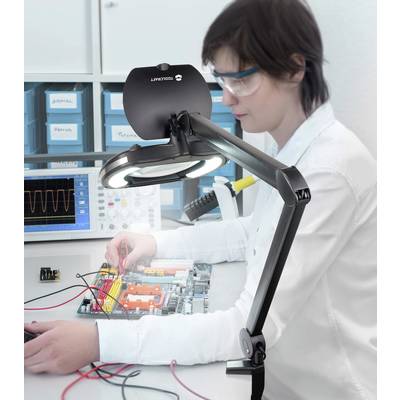 A person is working intently on a circuit with cables and circuit boards, surrounded by technical equipment and an oscilloscope.