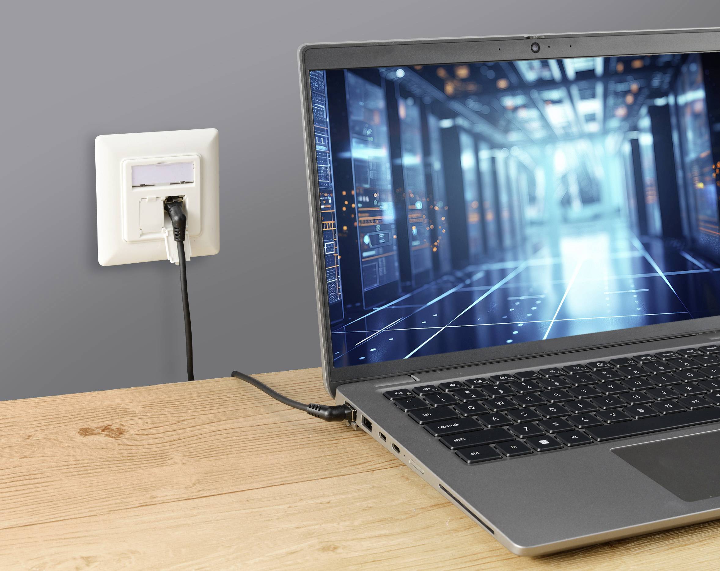 Laptop on a table, plugged into a power socket. A digital server room render is displayed on the laptop screen.