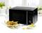 Black microwave on a white table, surrounded by pepper mill, salt mill, and a plate of nachos and guacamole.
