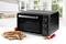 Compact black mini oven in a contemporary kitchen, with a pizza on a wooden board beside it.