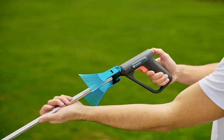 A person is using a grabber with a blue handle to pick up objects. The background is a green lawn.