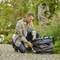 A man is kneeling outside on a paved path and preparing a grey Gardena compact collection bag to gather garden waste.
