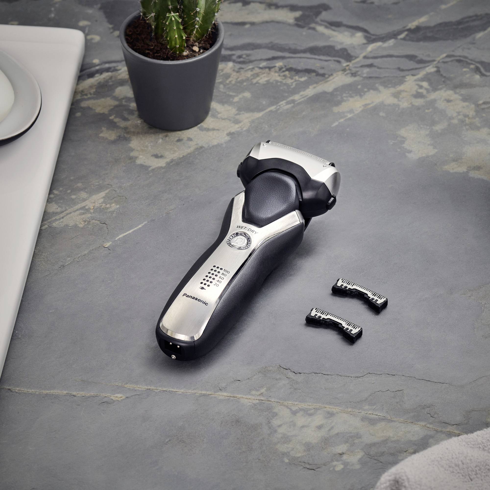 Electric razor on a grey bathroom surface next to a cactus and two spare blades.