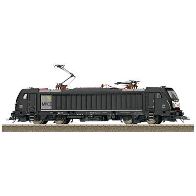 A black electric locomotive on rails, marked with 'MRCE', shows a side view with detailed running gear and pantograph.