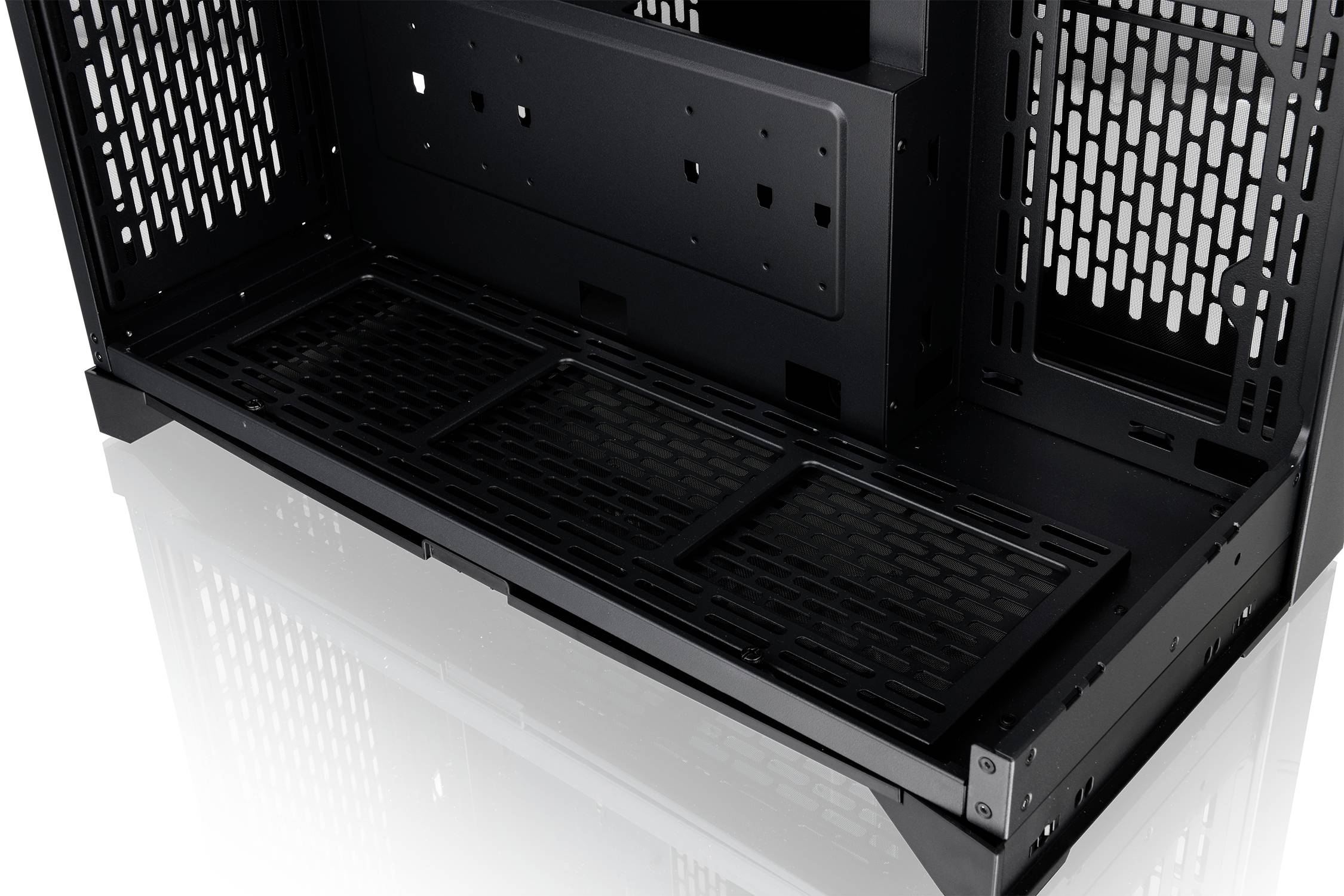 An empty, black computer case interior with multiple ventilation grilles and a reflective floor.