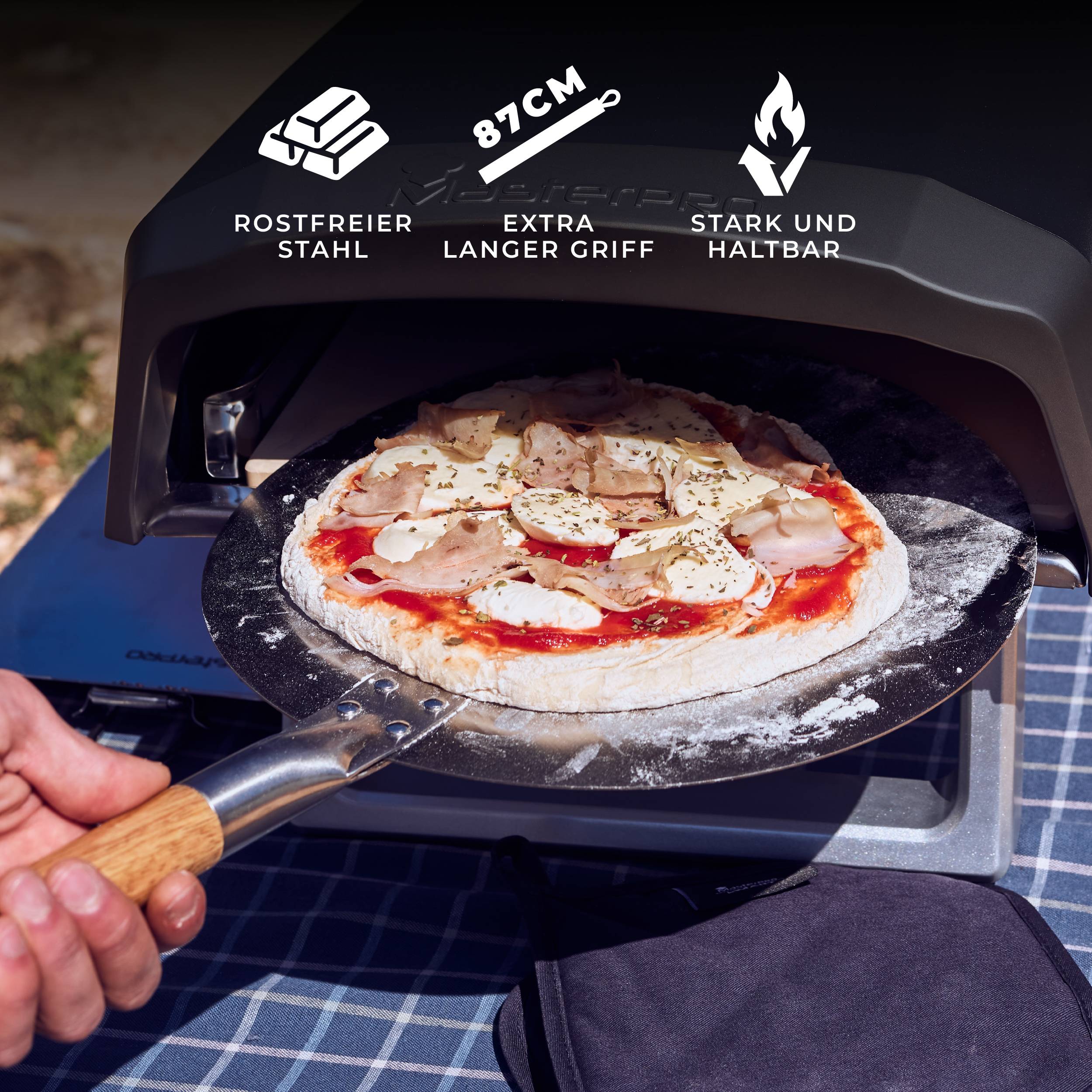 A person is sliding a pizza with mushrooms and mozzarella into a pizza oven, using a stainless steel pizza peel with an extra-long handle.