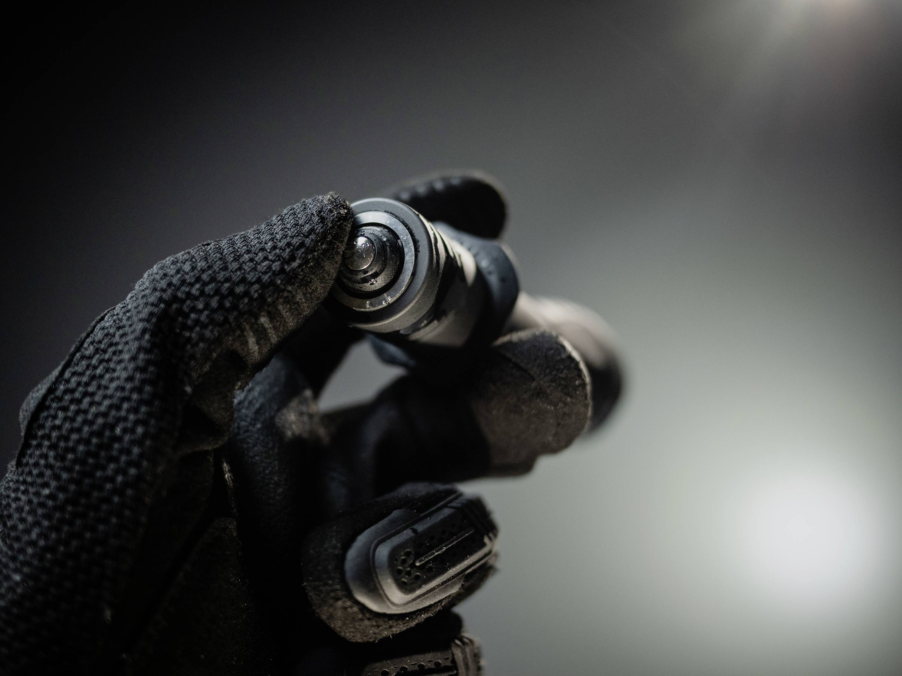 A gloved hand holds a small, technical device in front of a blurred background.