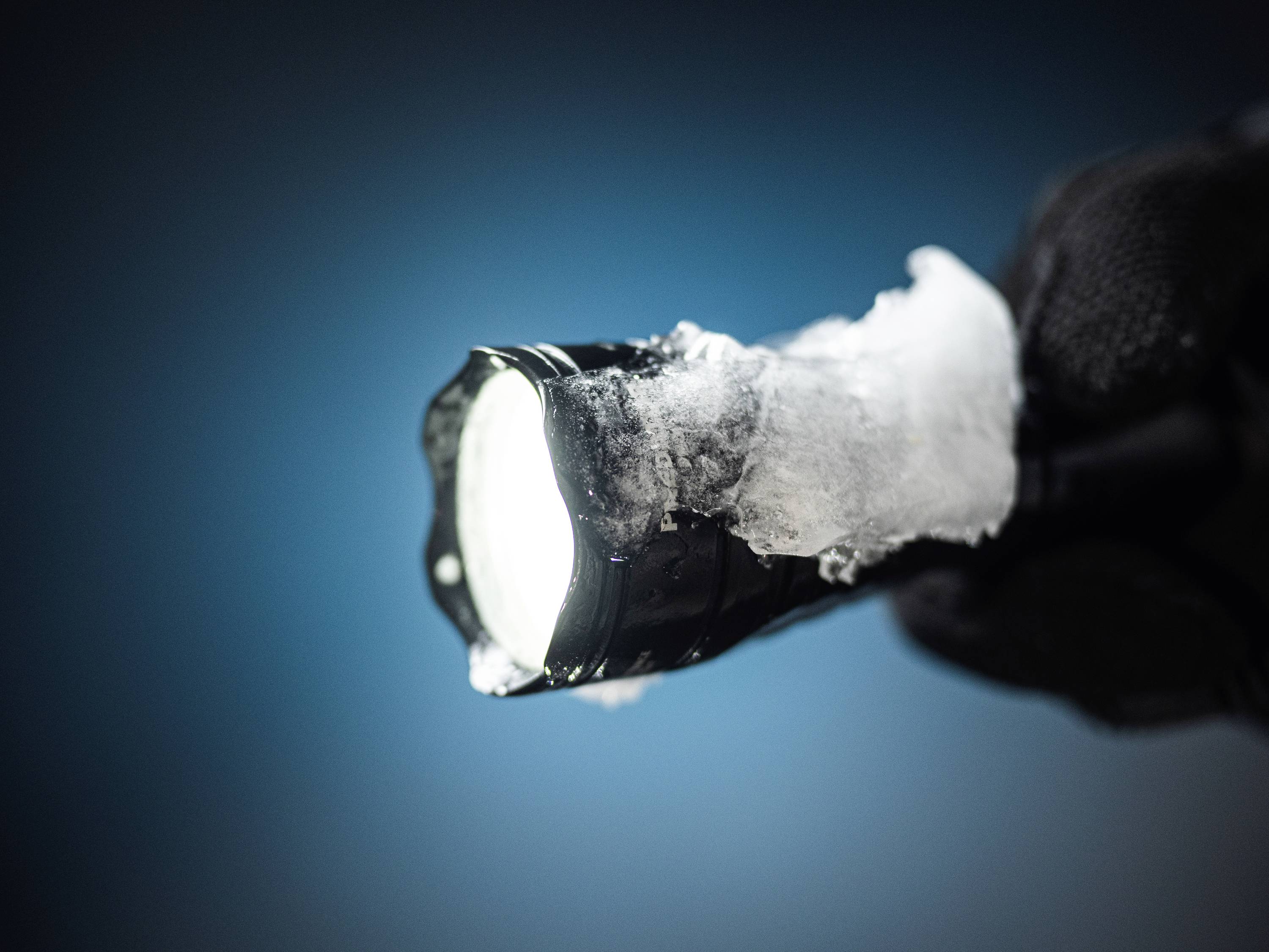A torch shines brightly, held by a gloved hand, partially covered in ice.