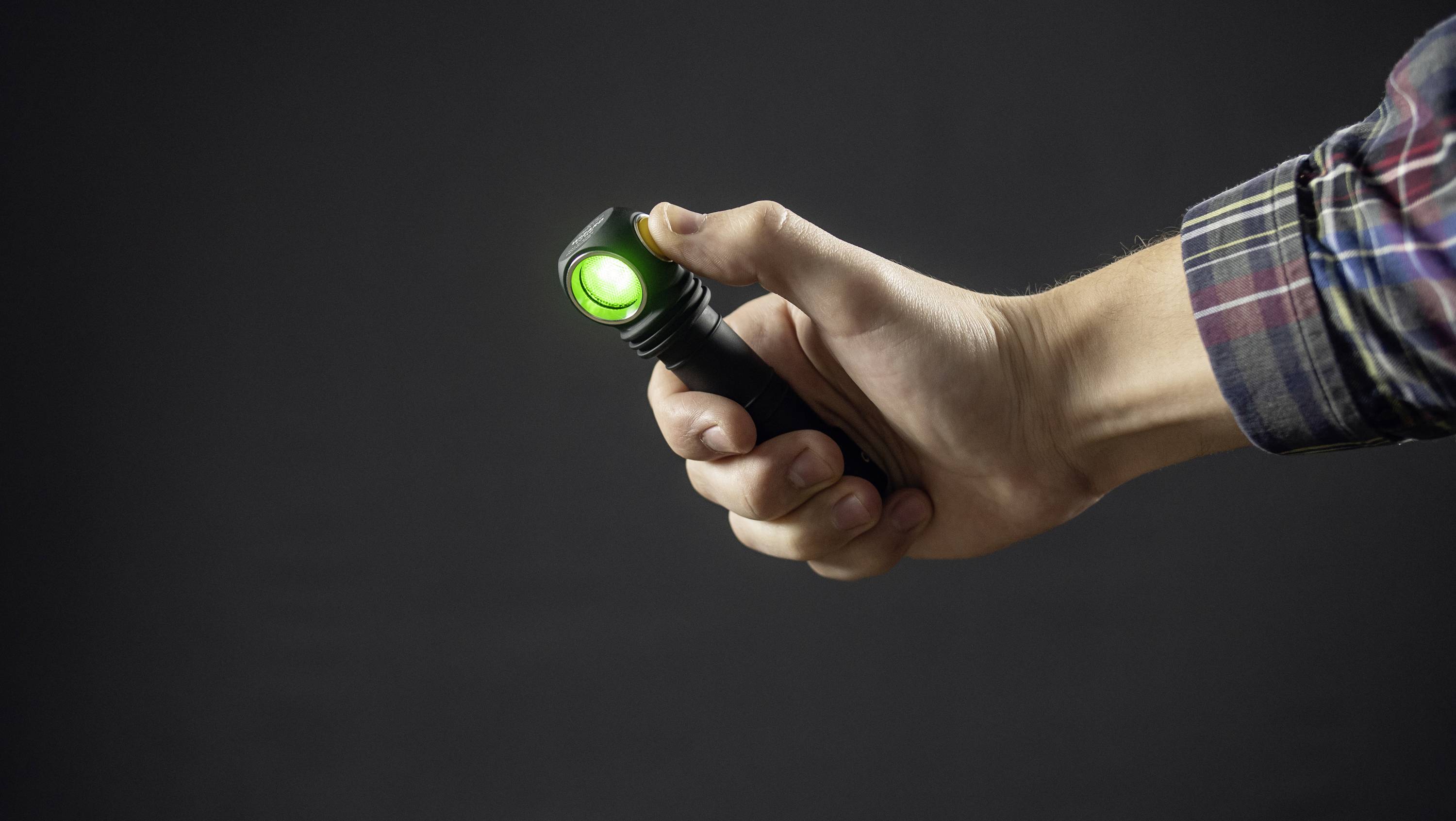 A hand holds a switched-on torch with green light against a dark background.
