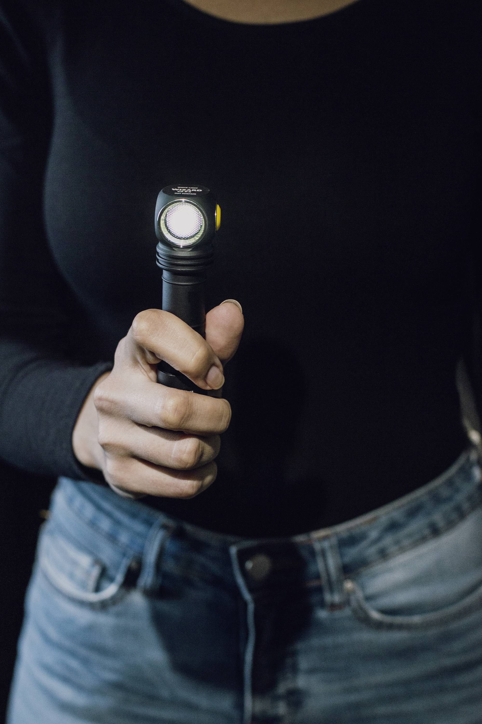 A person is holding a torch in their hand, which is switched on. They are wearing a black top and blue jeans.