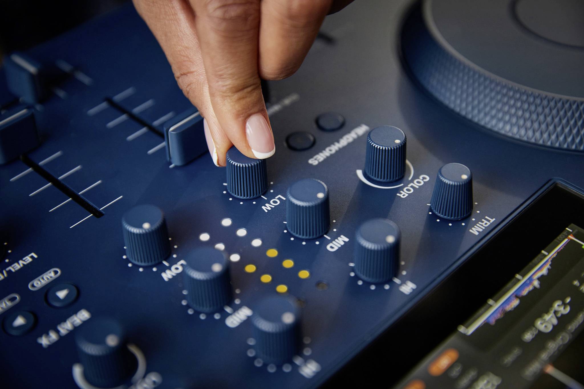 A hand turns a blue rotary knob on a DJ mixing desk to adjust the sound. Additional controls are visible in the background.