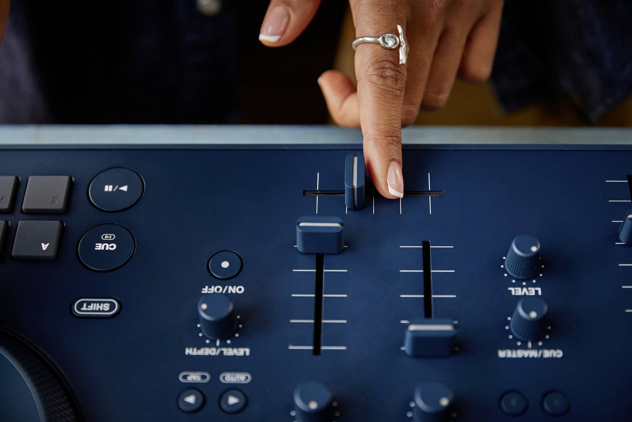 A person is operating a mixing desk, with fingers adjusting slider controls to manage volume or sound. The control interface has multiple rotary knobs.
