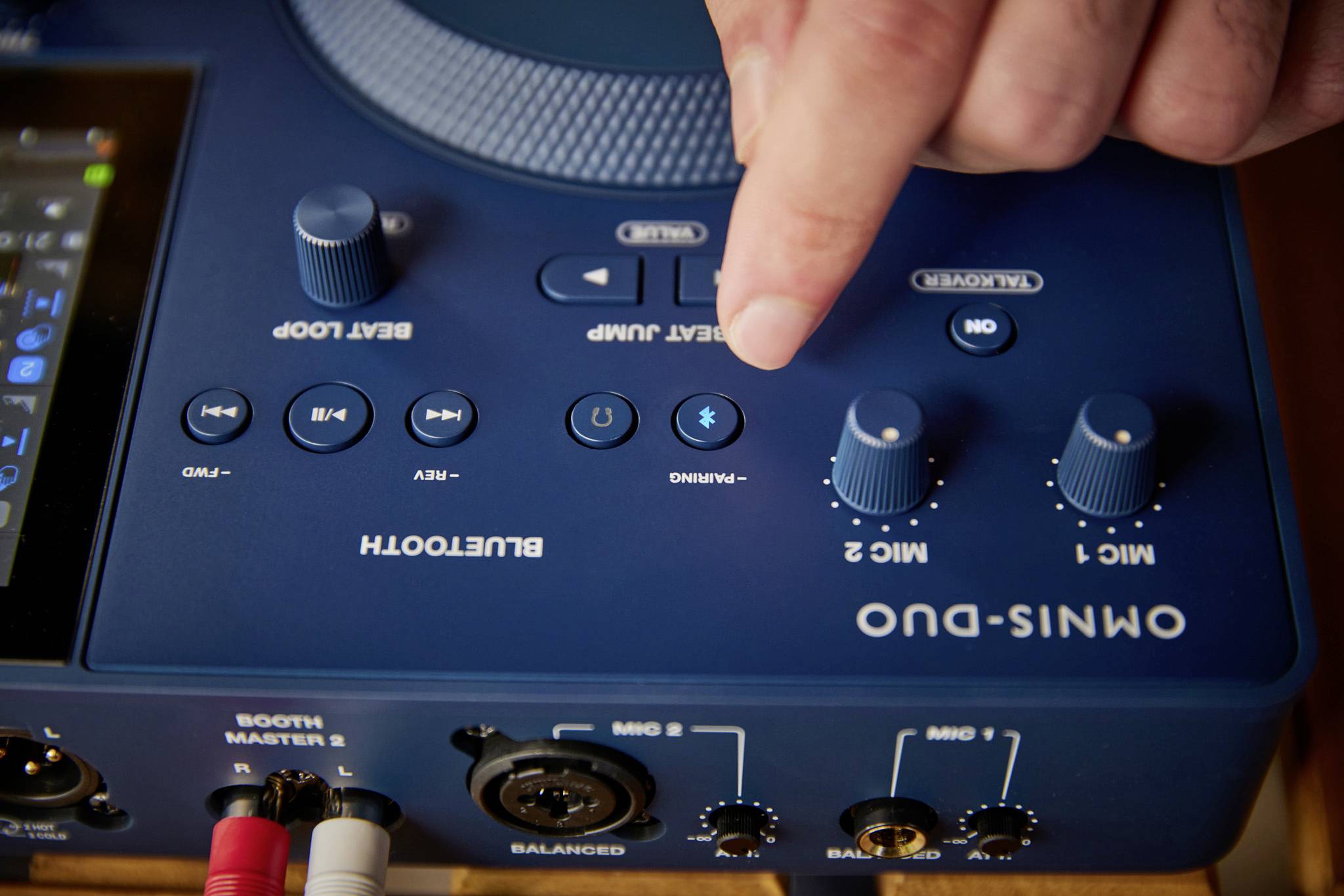 A hand turns the 'Mic 2' control on a blue mixing desk with Bluetooth and various control elements.