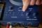 A hand turns the 'Mic 2' control on a blue mixing desk with Bluetooth and various control elements.