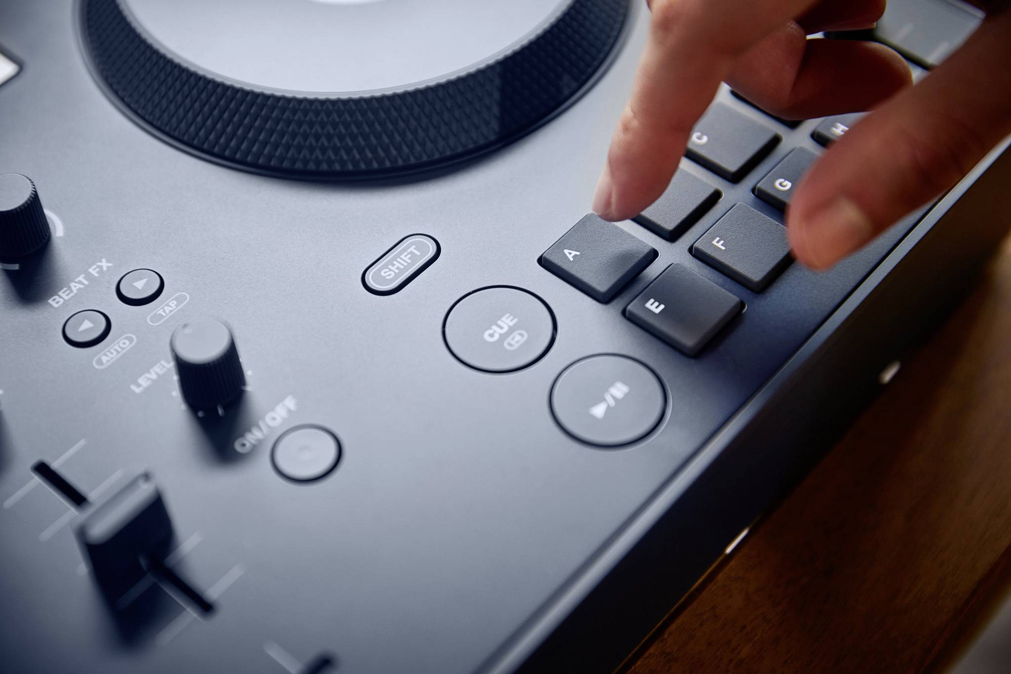 A finger presses a button on a DJ mixing desk. Beside it are additional buttons and controls for managing the music.