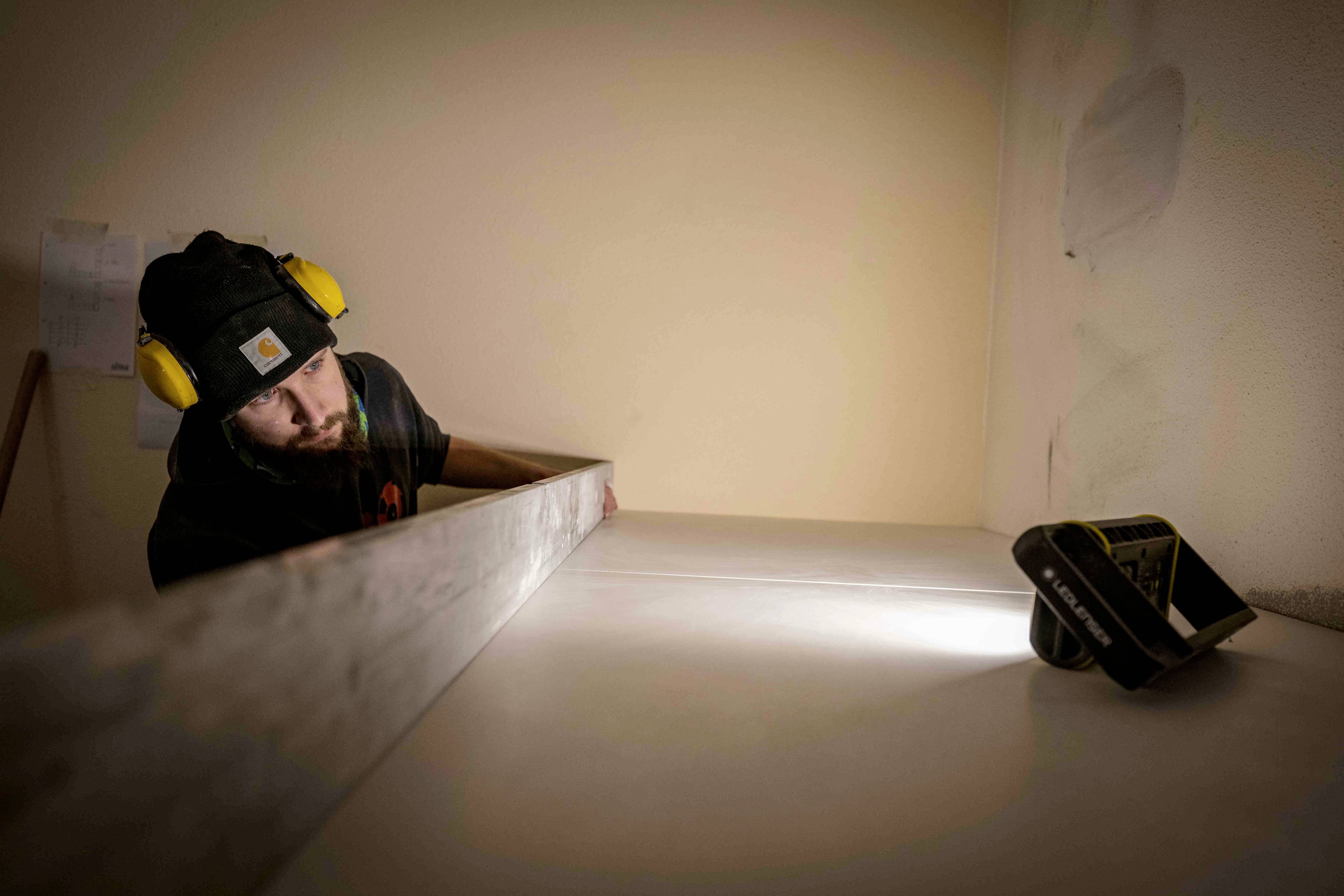 A man wearing ear defenders is measuring a shelf with a spirit level in a room. He is focused on his work.