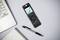 Digital dictaphone with display lies beside a laptop, pen and notepad on a table. Device shows recording information.