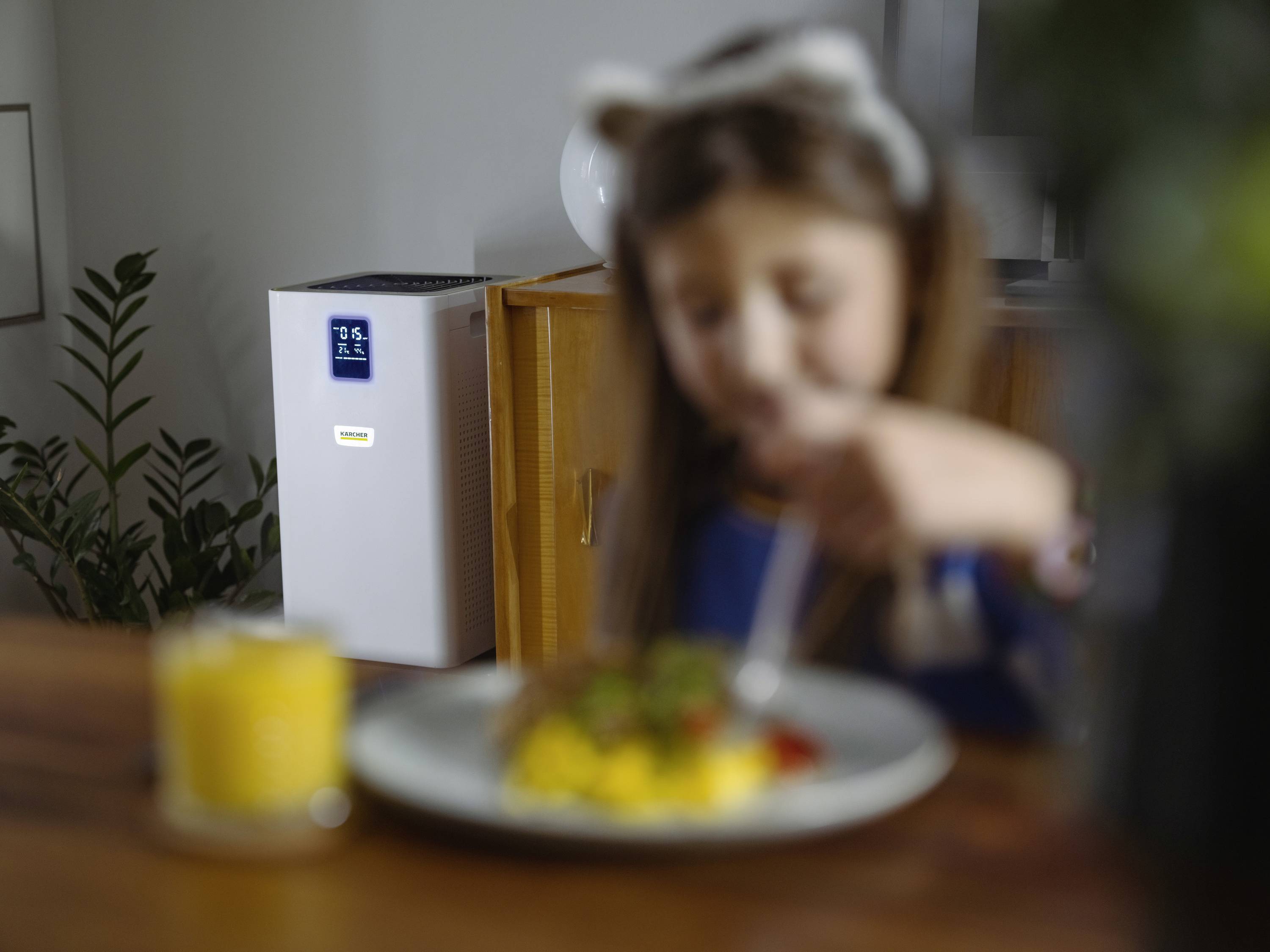 A child is eating at the table, with an air purifier with its display switched on in the background.