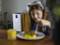 A child is eating at the table, with an air purifier with its display switched on in the background.