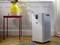 An air purifier stands on a wooden floor next to a small table with a flower-filled vase, surrounded by natural light.