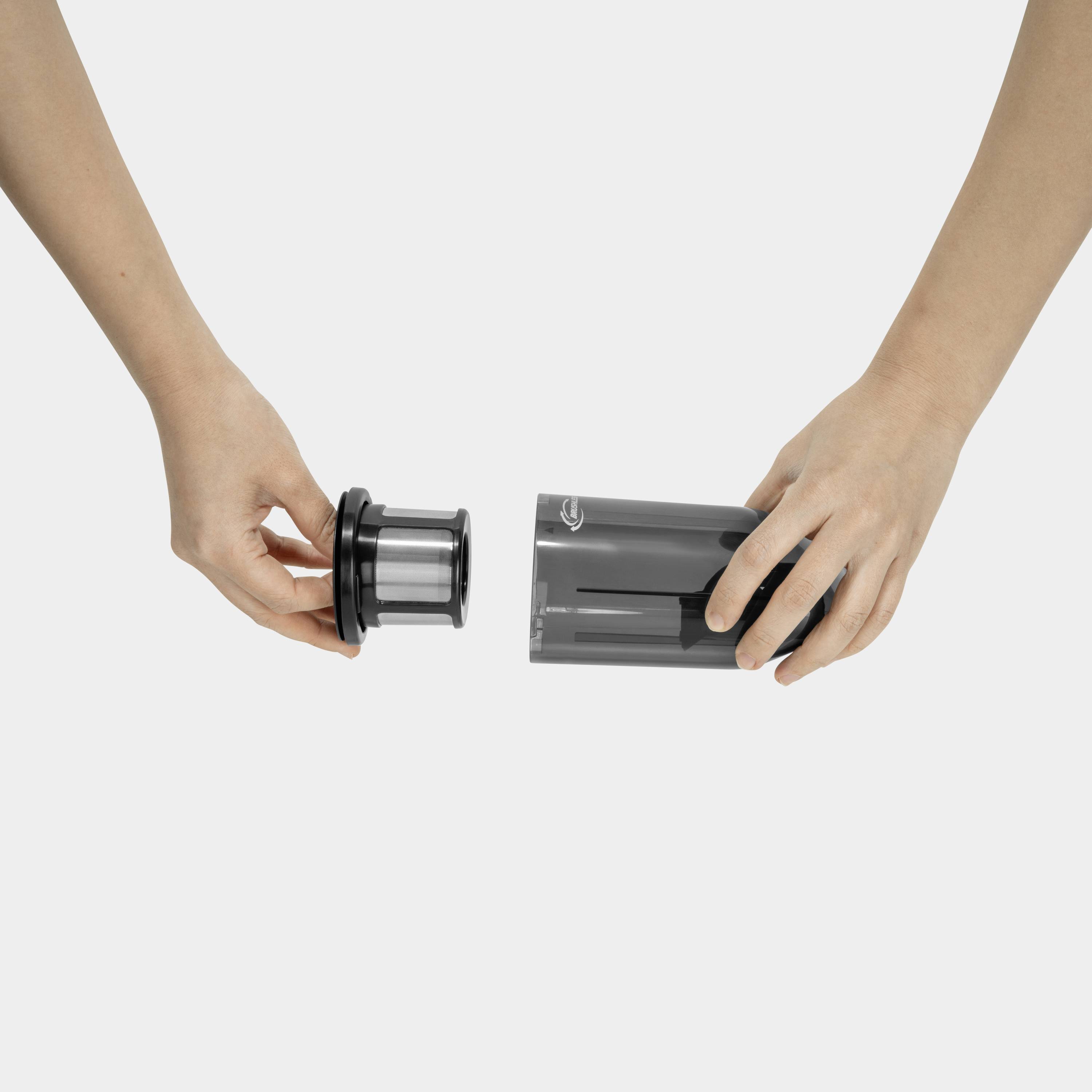 Two hands assembling parts of a coffee machine. The right hand is holding a transparent container, while the left hand holds the filter unit.