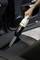 A hand is using a small, portable vacuum cleaner to remove dirt from between the seats of a car.