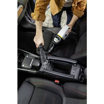 A person is vacuuming a car interior with a portable hoover. Focus is on cleaning the centre console between the front seats.