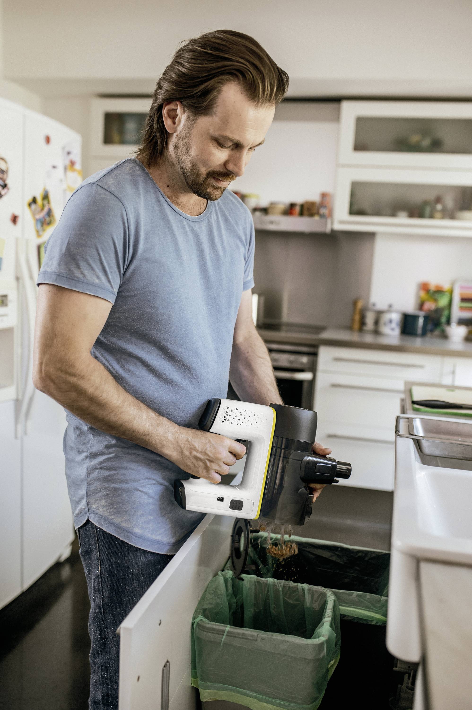 A man is using a kitchen appliance to dispose of waste over a rubbish bin in a modern kitchen.