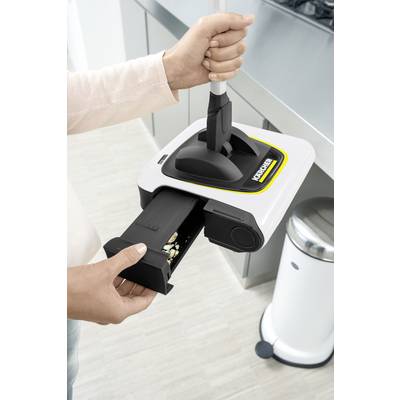 A person is emptying a small vacuum cleaner container over a rubbish bin in a bright kitchen.