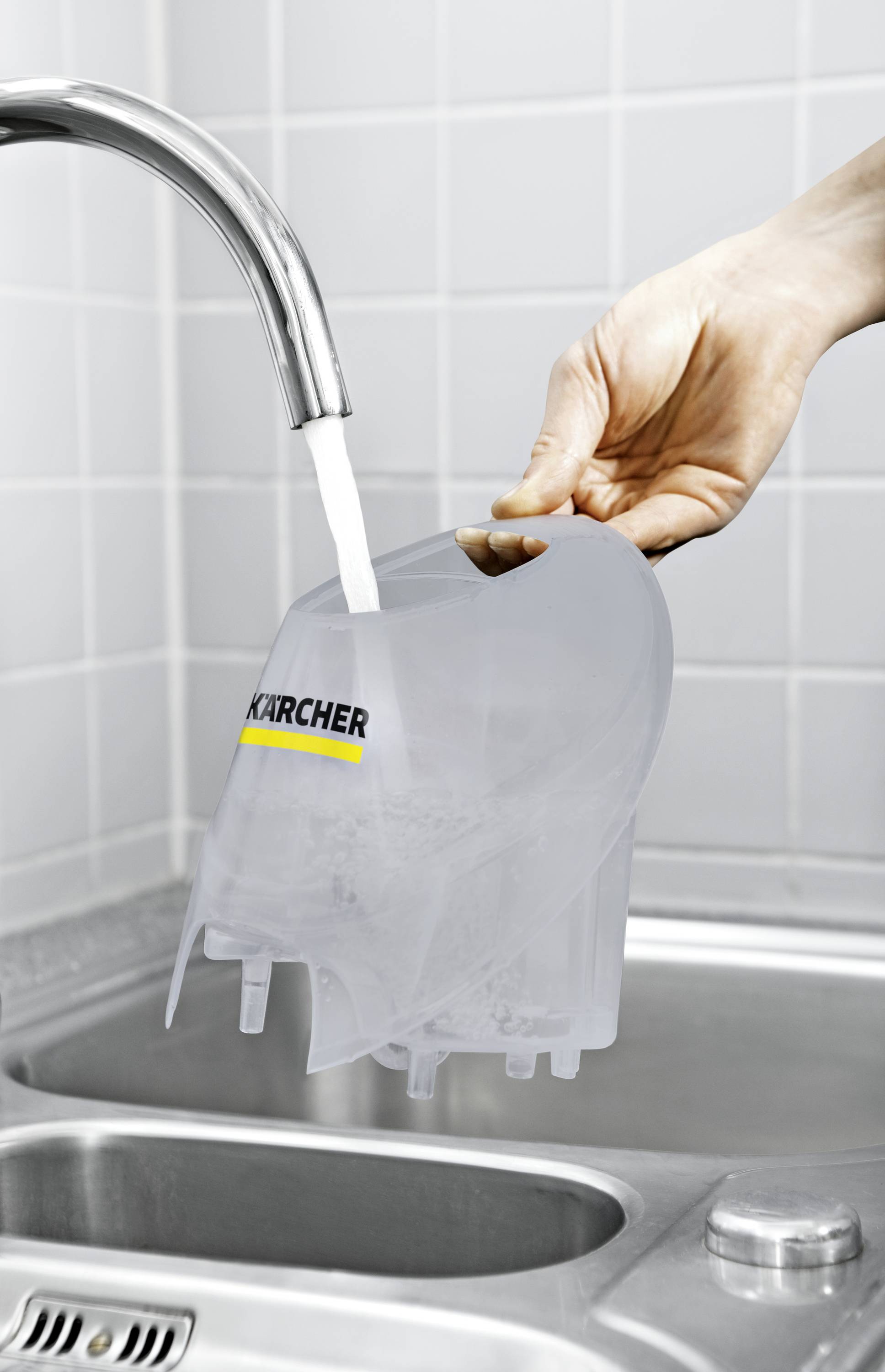A hand holds a grey water tank under running water from a tap in a kitchen sink.